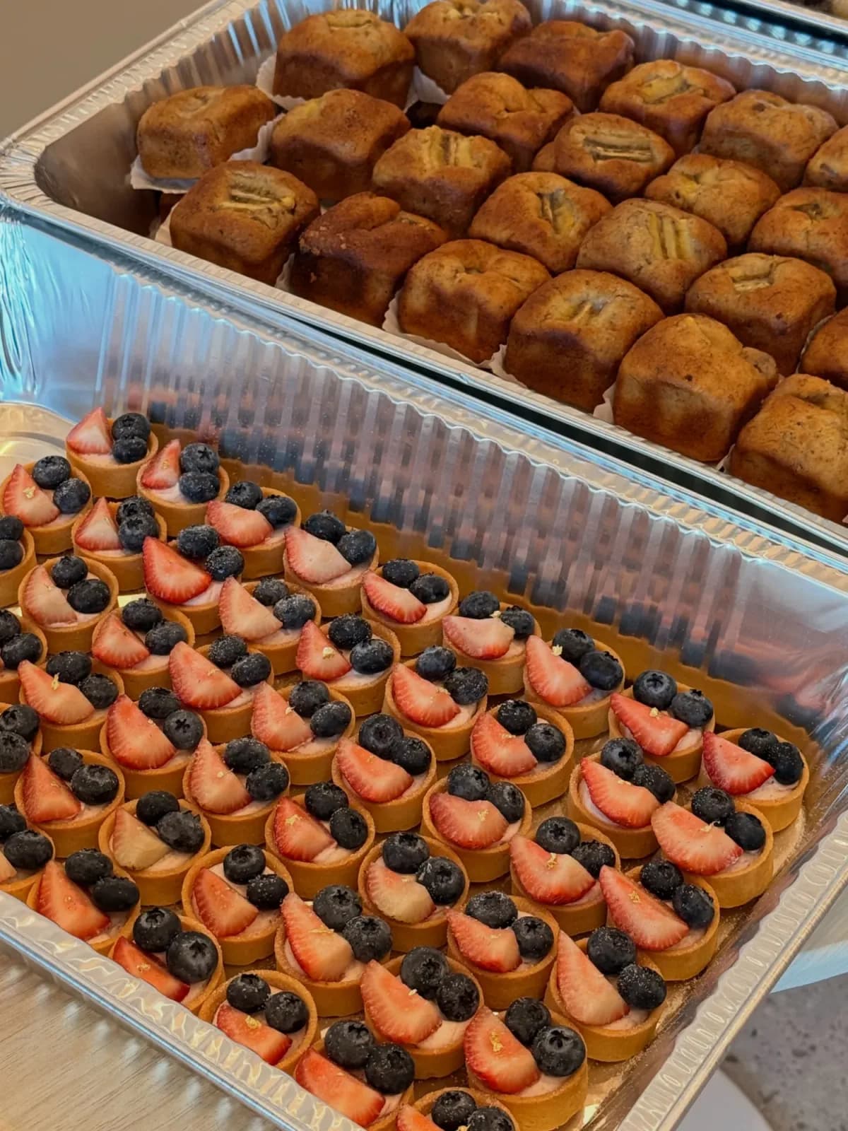 Catering trays packed with mini banana loaves and dozens of berry tartlets