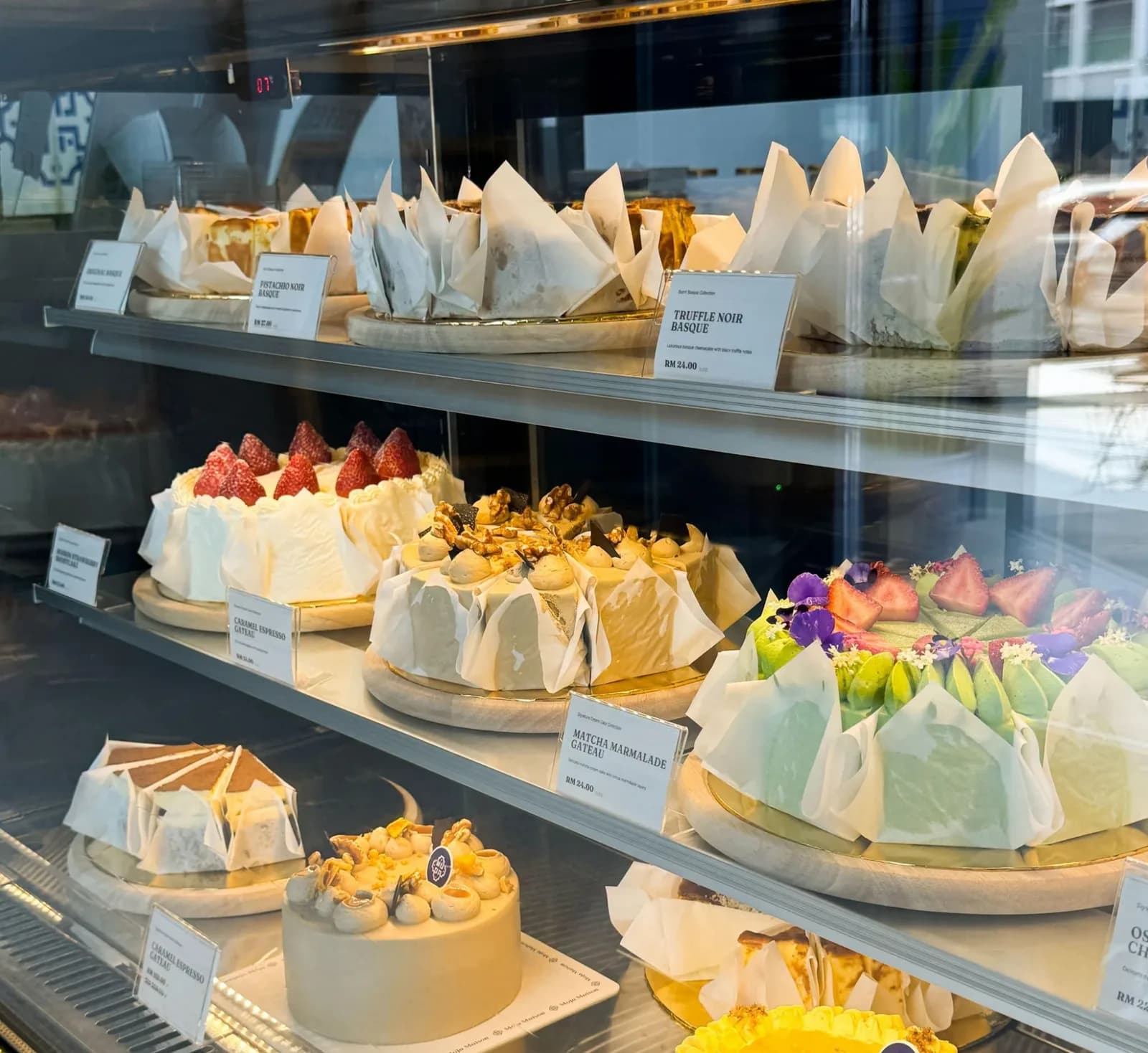Moja Maison retail display case with labelled cakes and cheesecakes on two shelves
