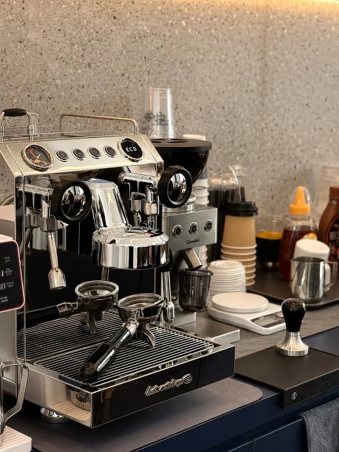 Espresso machine and grinder on the Moja Maison coffee bar, with cups and a tamper ready for service