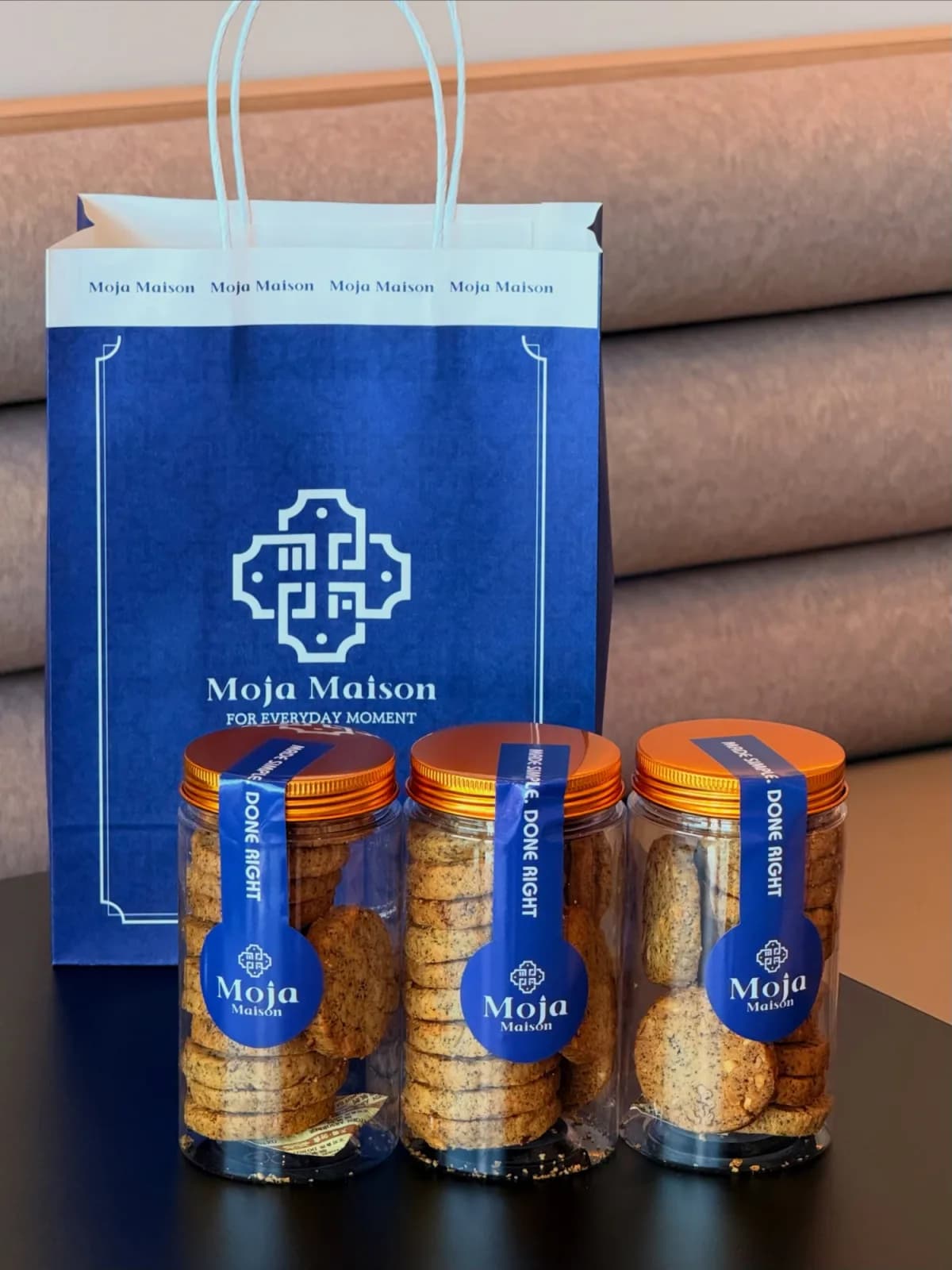 Three ribboned Moja Maison cookie jars in front of a branded navy gift bag